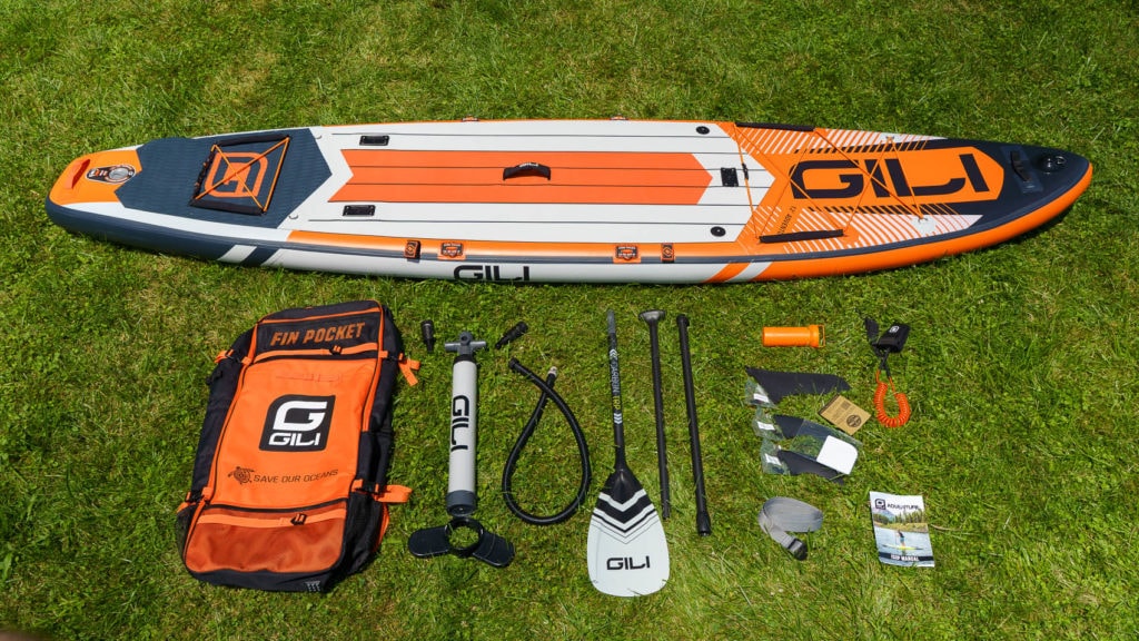 Unboxing the orange GILI Adventure SUP accessories, including bag, single chamber compact pump, carbon TRP, 3 fins, repair kit, SUP leash, compression strap, and documentation.